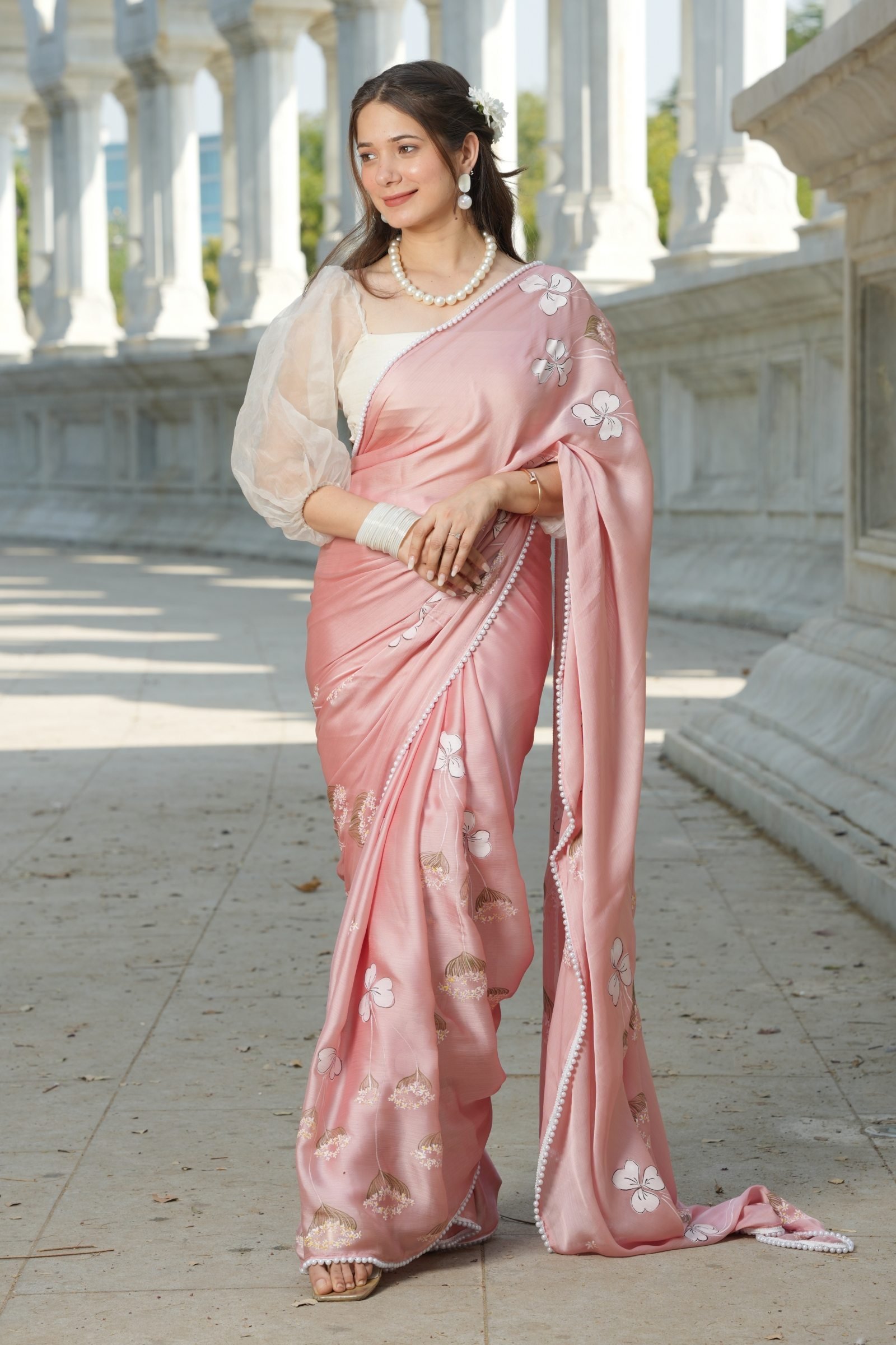 Indian woman posing in Blush Blossom Pure Silk Saree, showing the flowing fabric and white handpainted flowers.